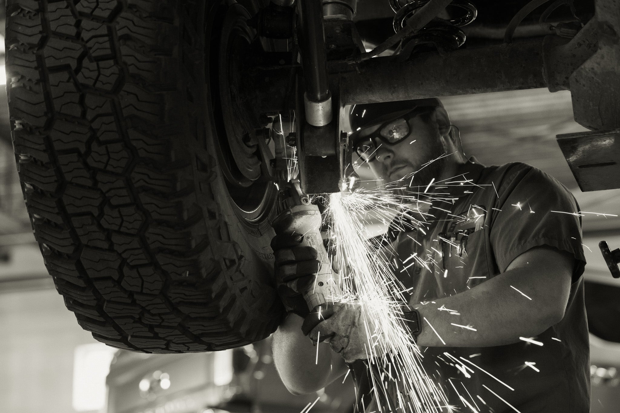 man grinding component under car wearing safety glasses