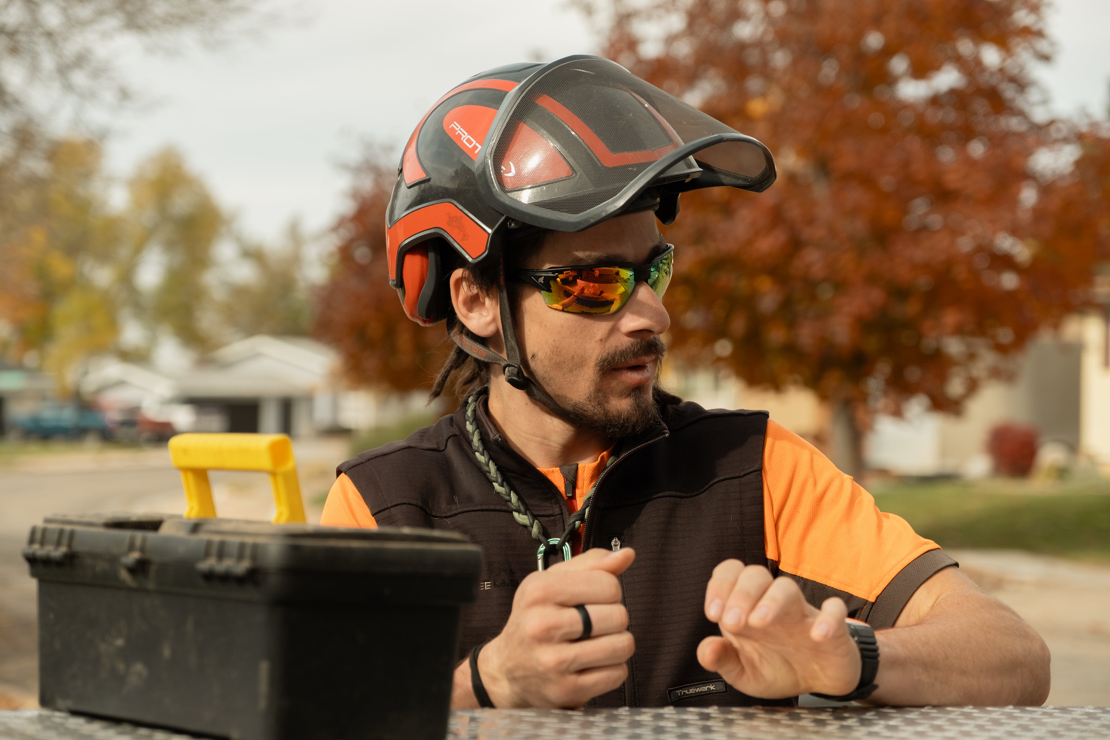 Person wearing a helmet and sunglasses sitting outdoors with a tool box in front