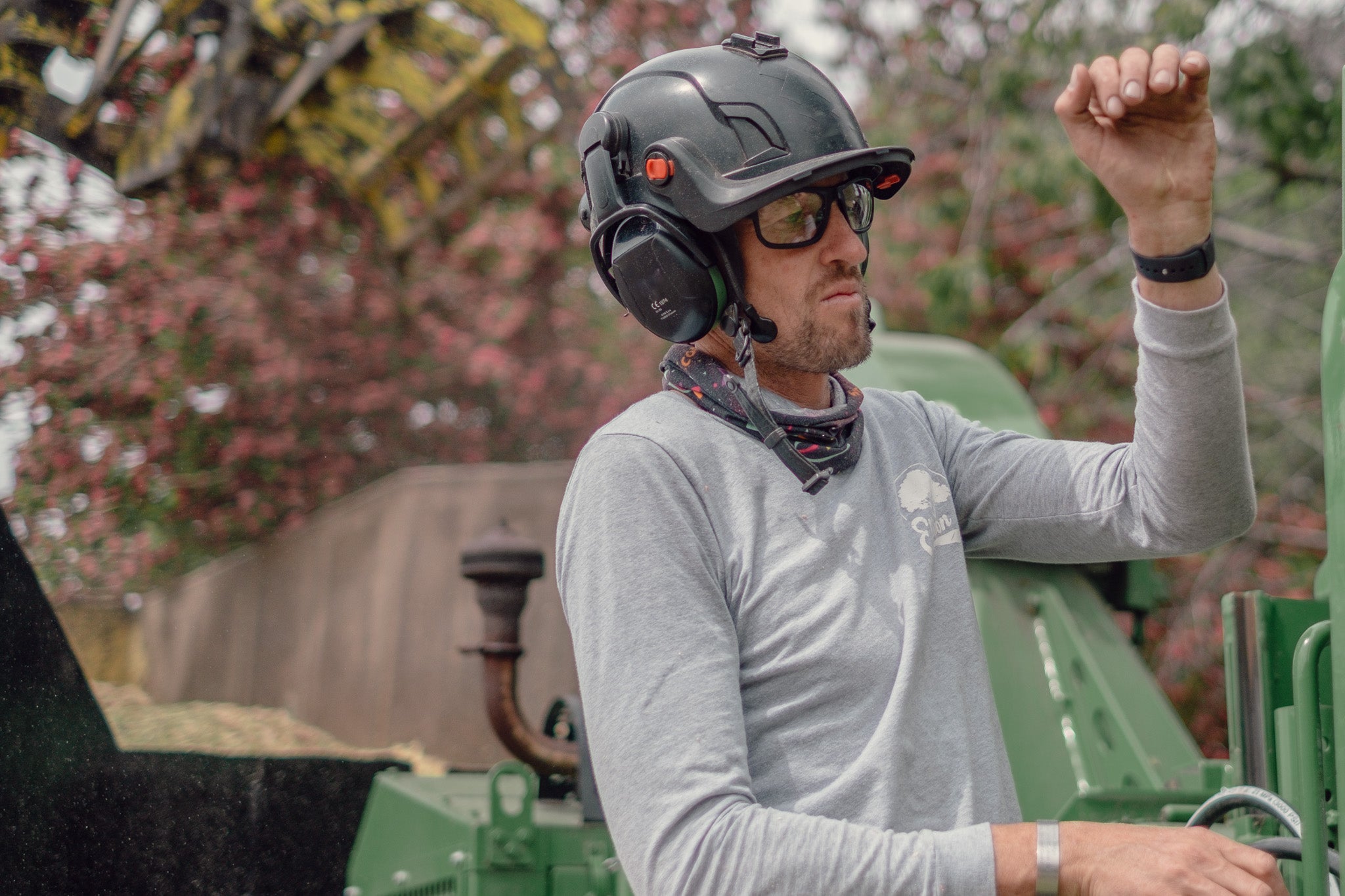 Person wearing a helmet and safety glasses operating machinery with a blurred natural background