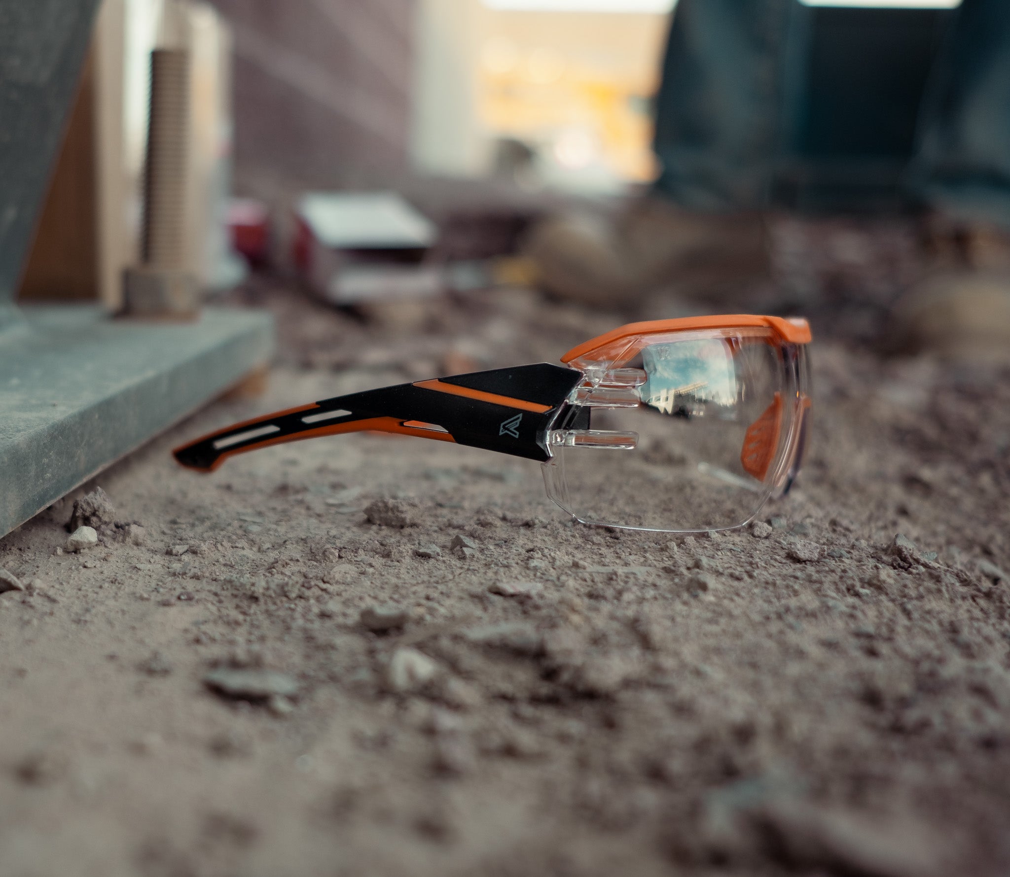 clear safety glasses sitting on ground near metal structure with a man's boots in the background. 