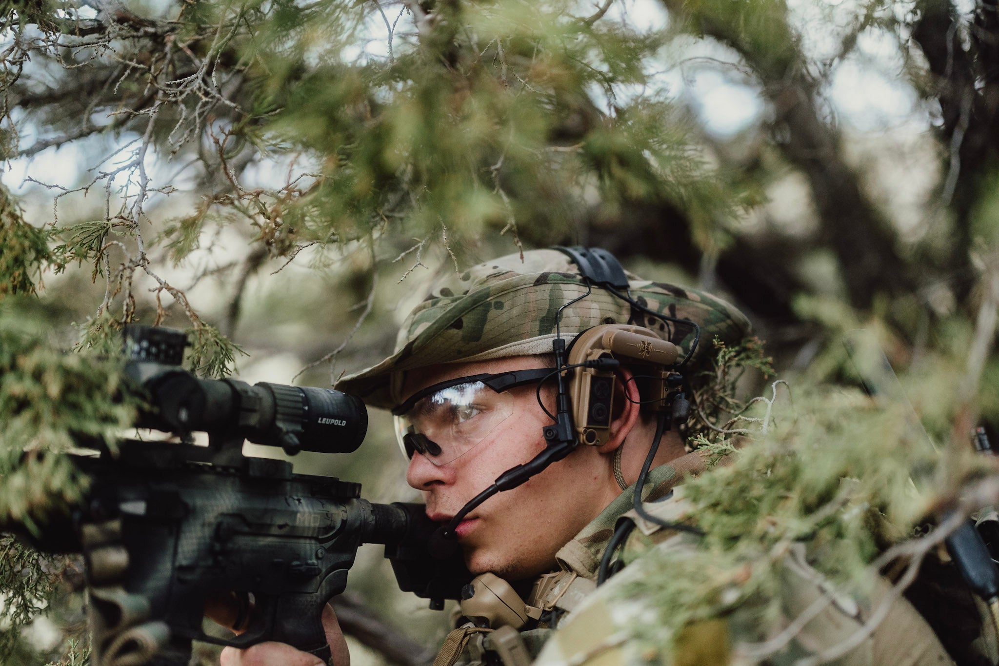 Person in camouflage gear with a rifle in a forest setting