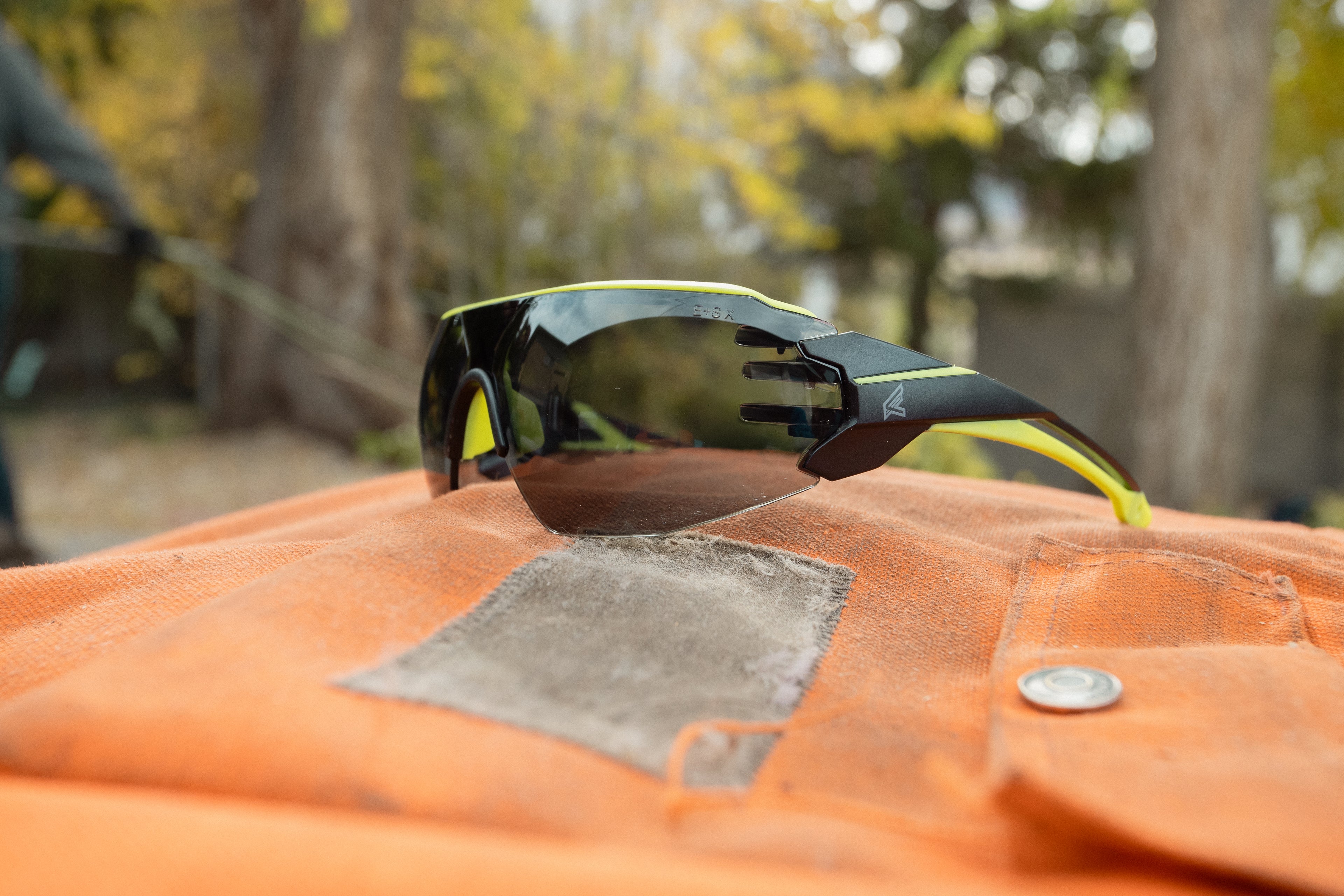 Black safety glasses with yellow accents on chainsaw apron outside