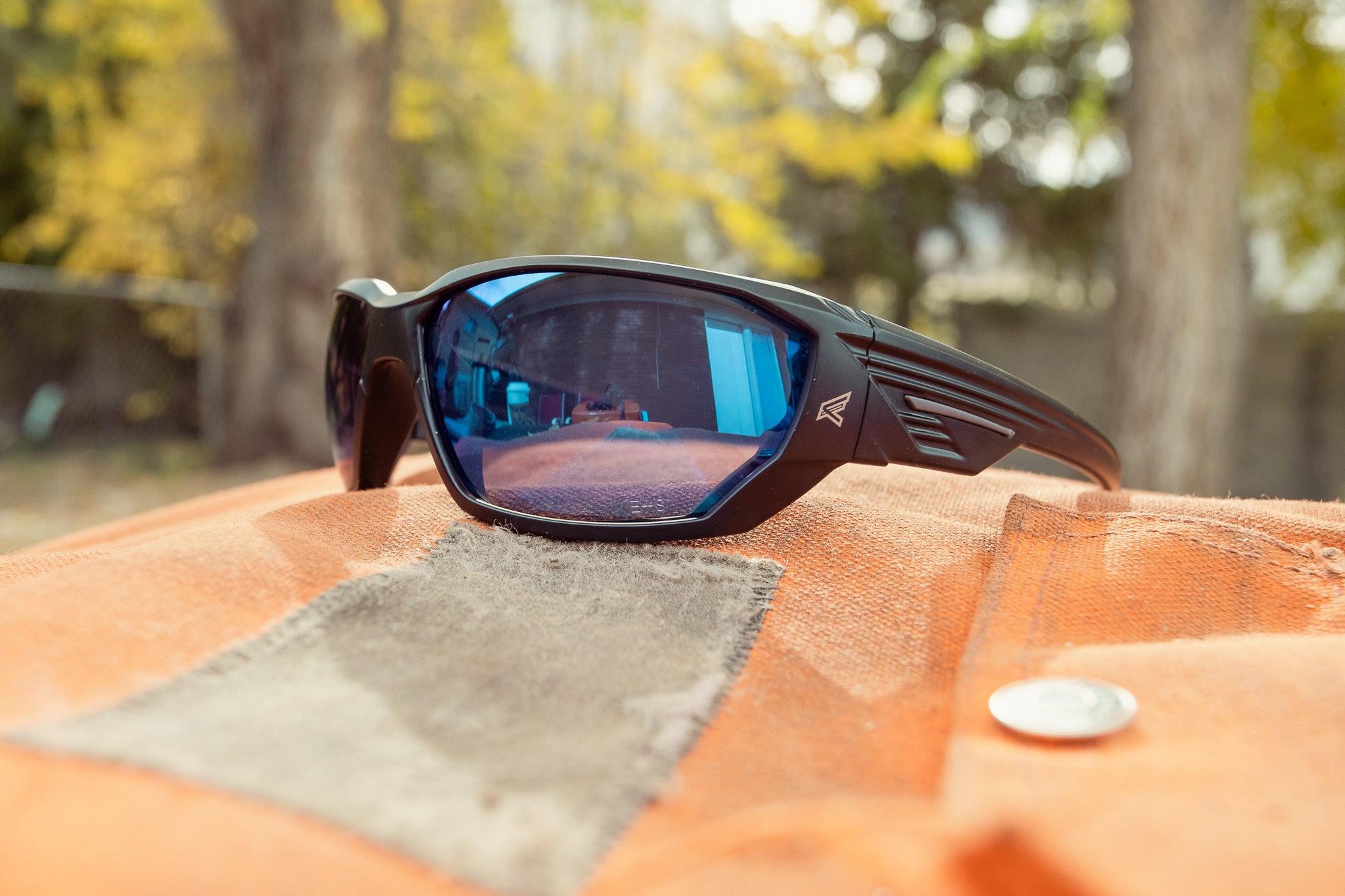 Sunglasses with blue lenses on a textured surface with blurred natural background