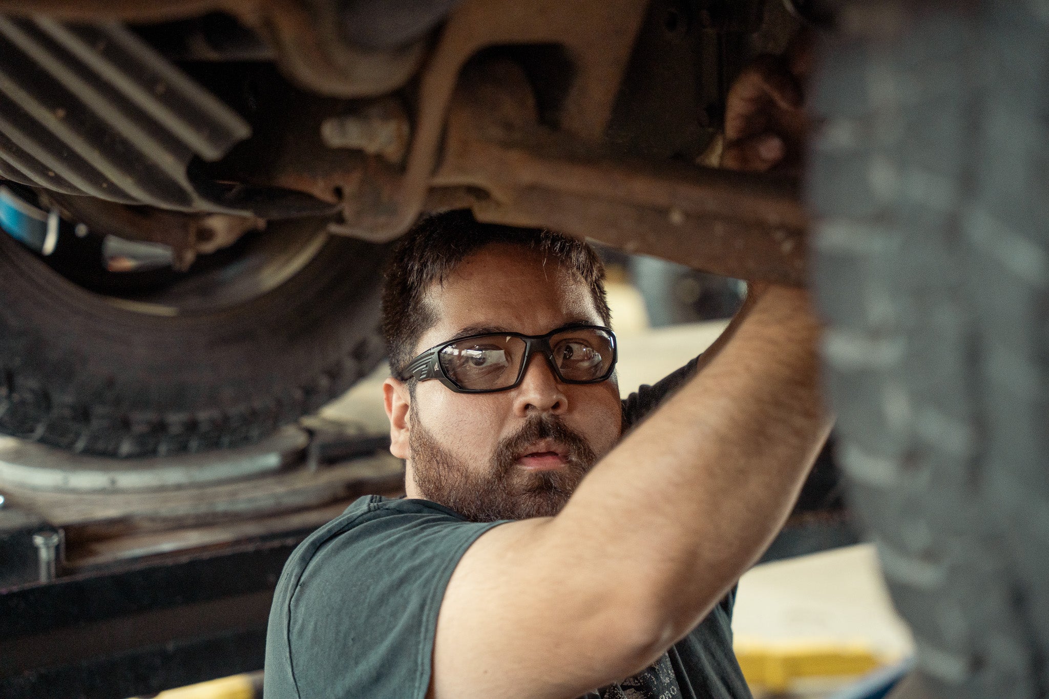 Man working on a vehicle undercarriage and wearing safety glasses