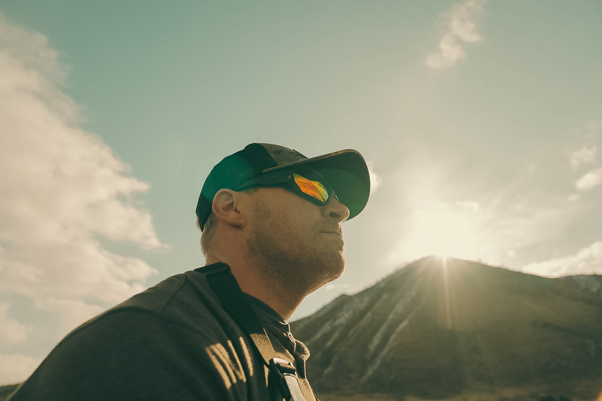 Person wearing a cap and sunglasses with mountains in the background