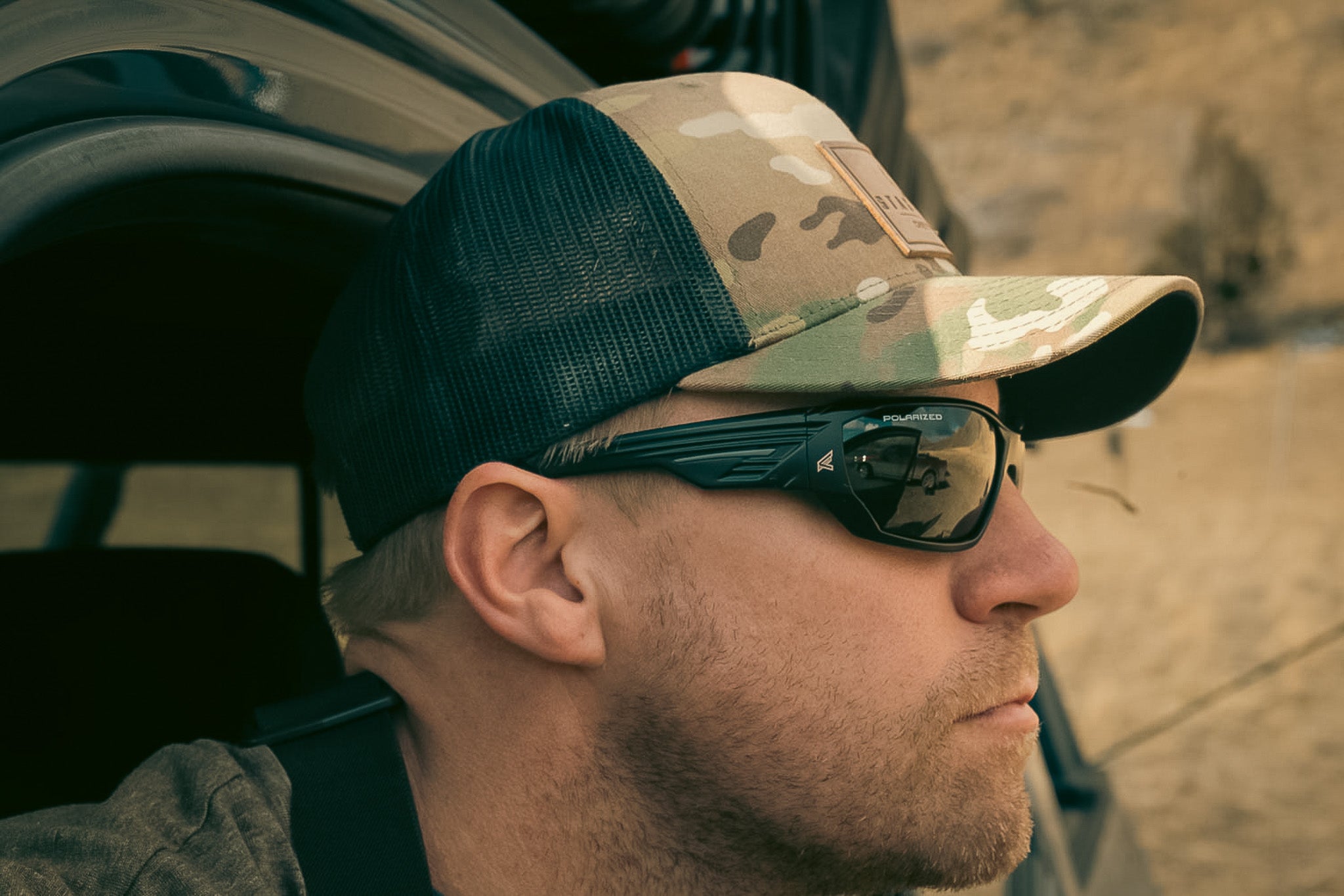Man wearing a camouflage baseball cap and safety sunglasses in a desert setting