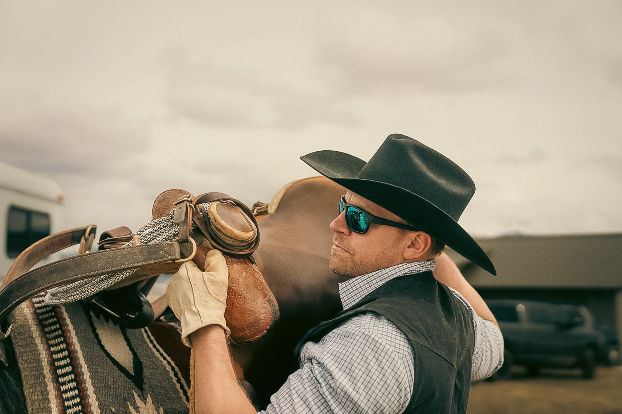 man wearing cowboy hat and blue lens safety glasses by horse