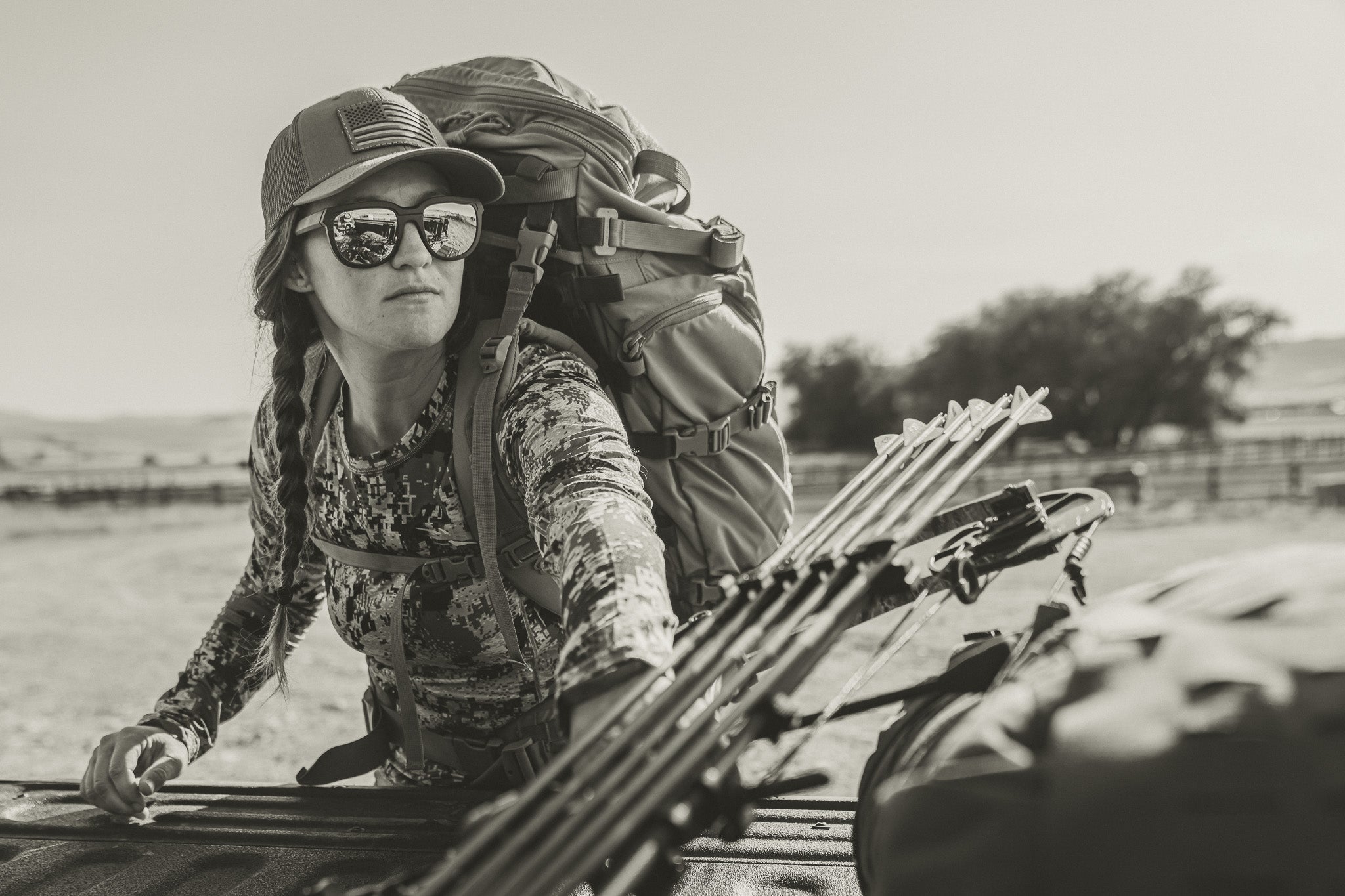 Person with camouflage clothing and archery equipment in a desert setting wearing sunglasses.