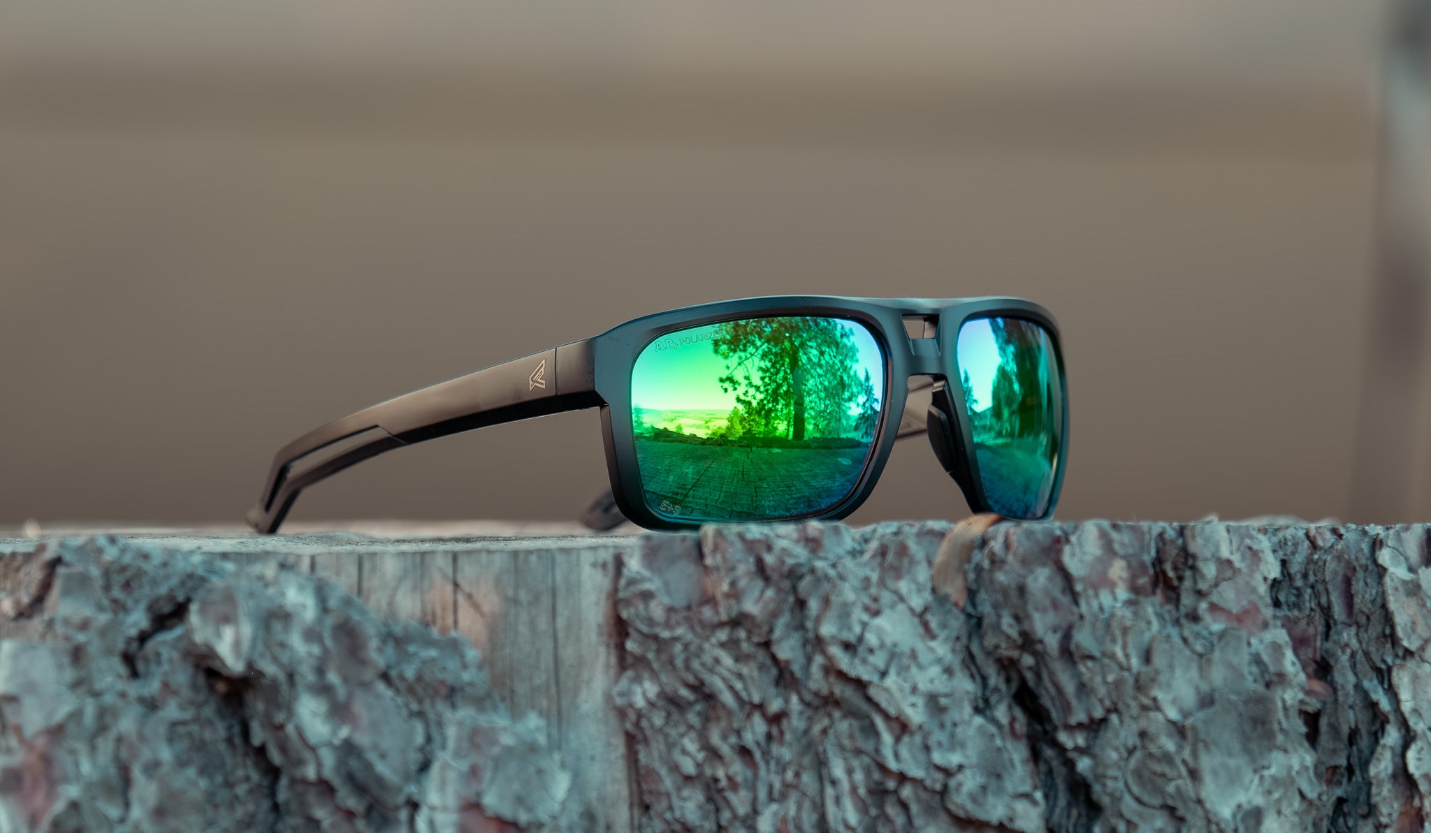 green lens safety glasses sitting on log in outdoor setting. 