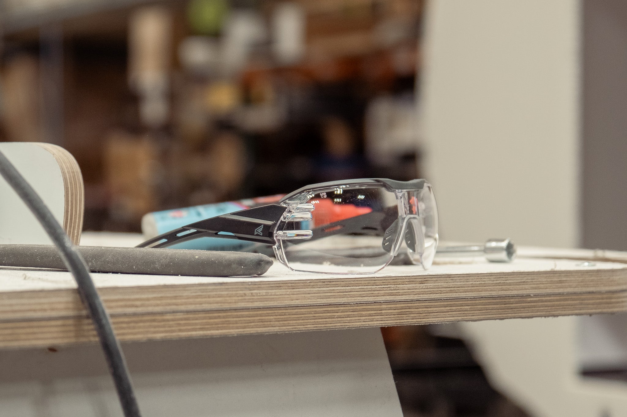 Clear safety glasses sitting on workshop table with tools in the foreground.
