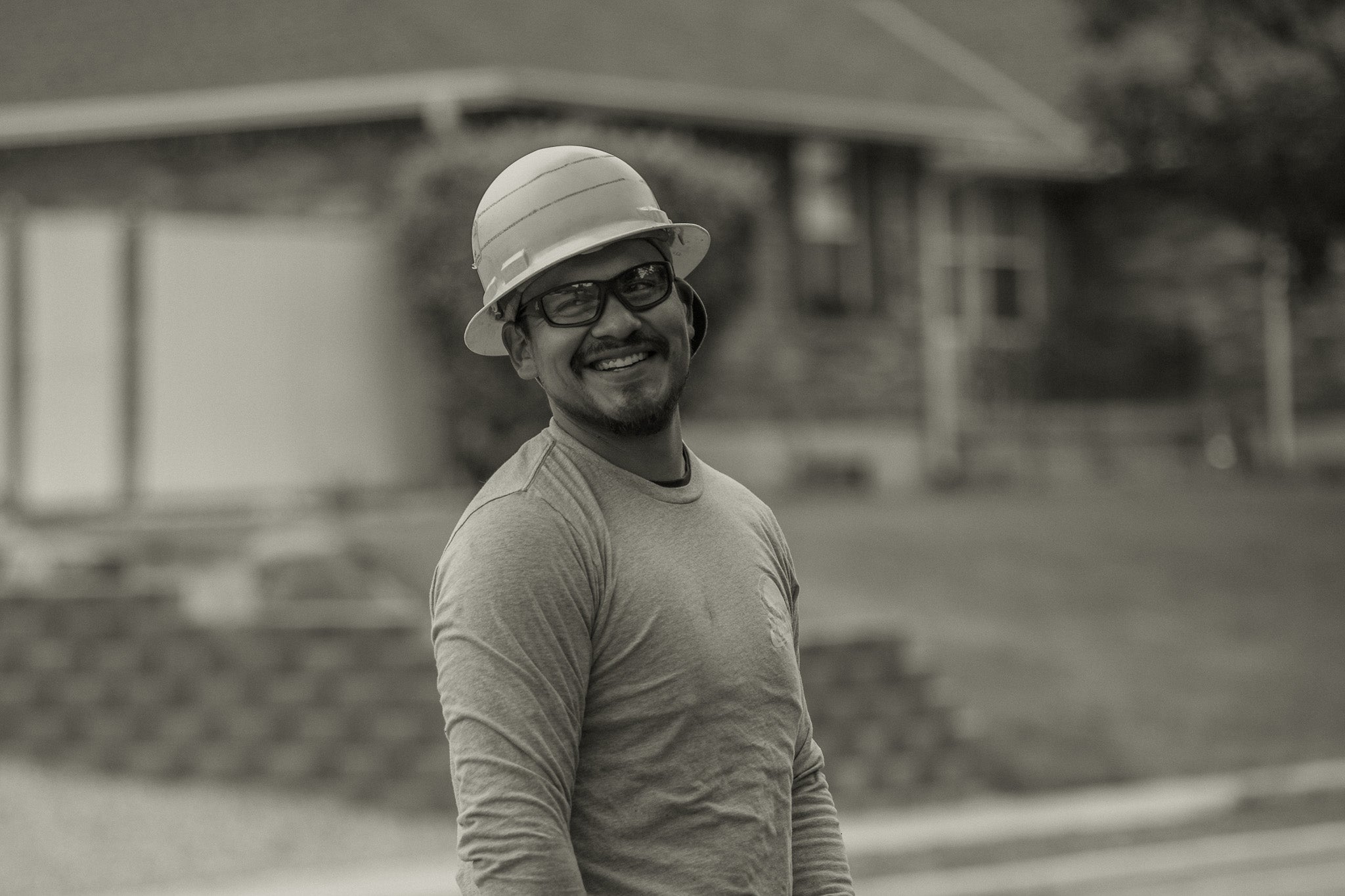 Man wearing a hat and glasses standing outdoors with a blurred background