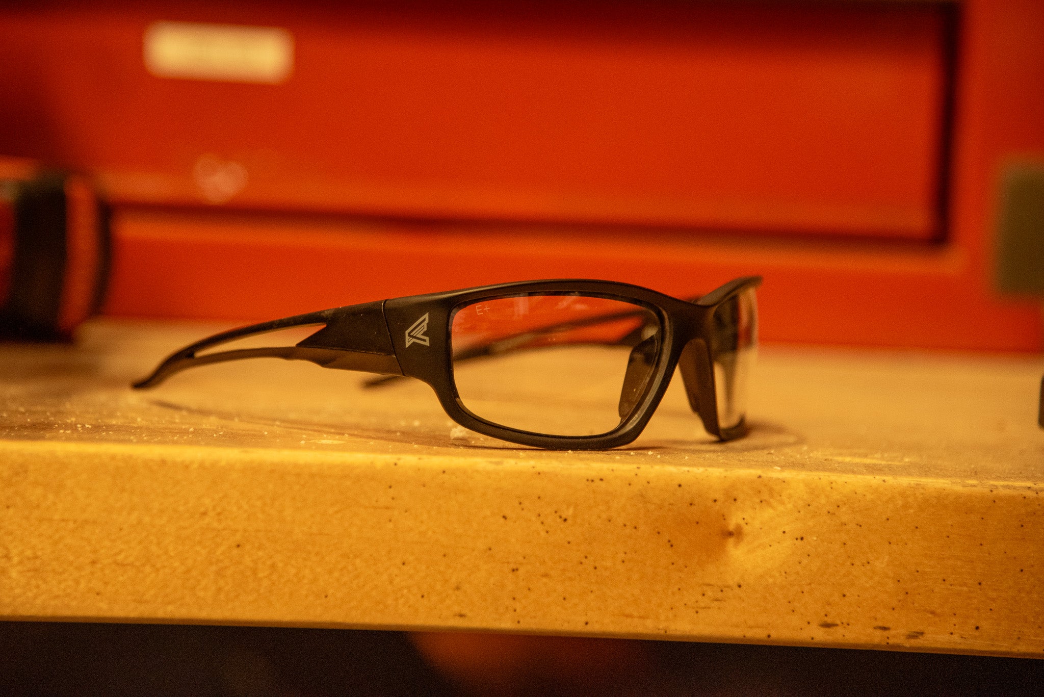 Black safety glasses on a wooden surface with a red background