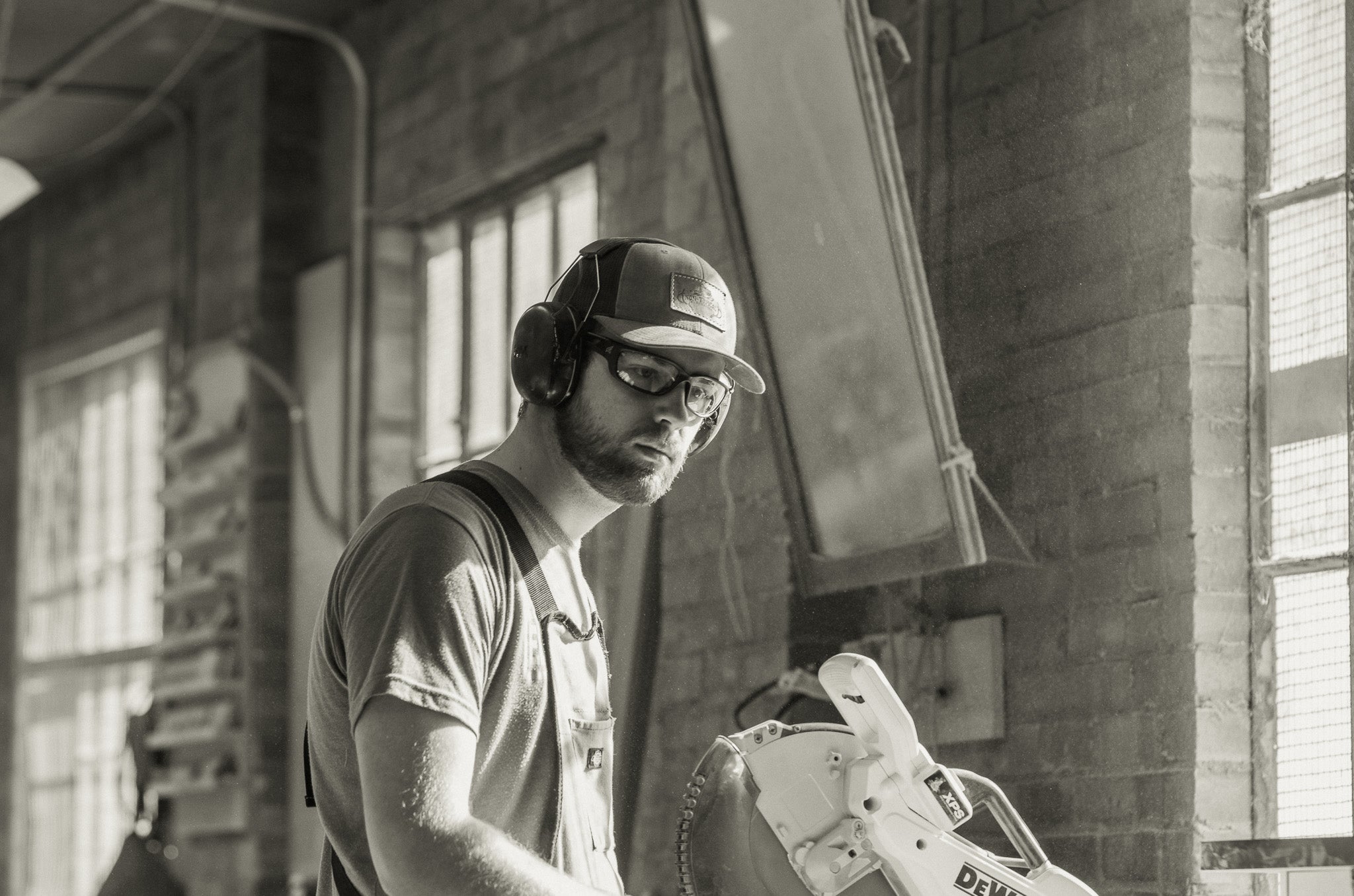 Man operating a saw indoors with a brick wall background