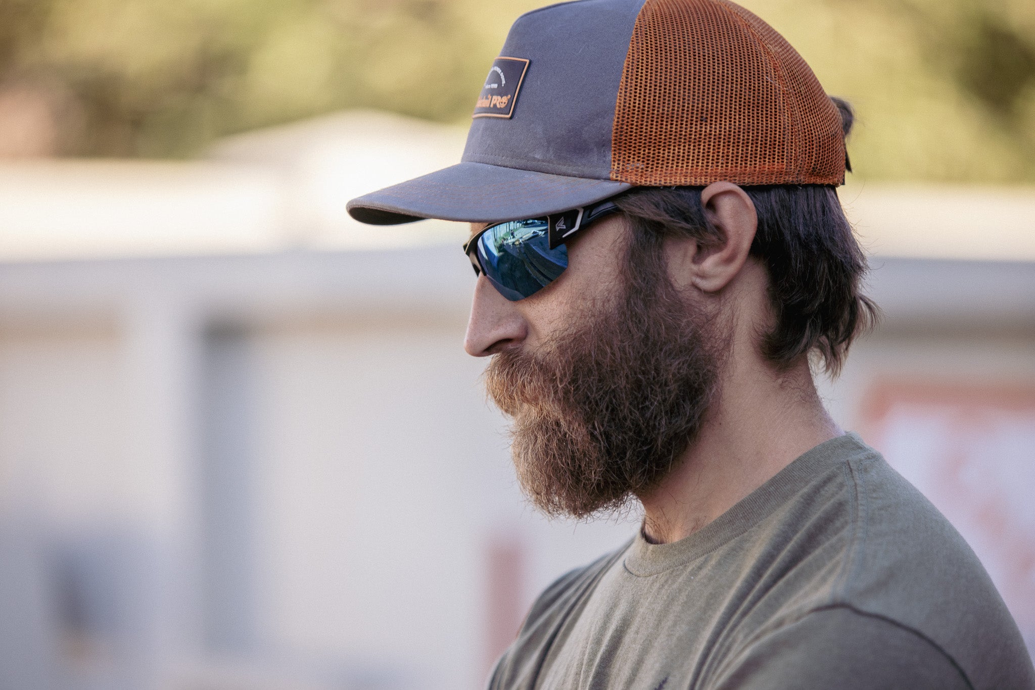 Man wearing a brown and blue cap with safety sunglasses, outdoors.