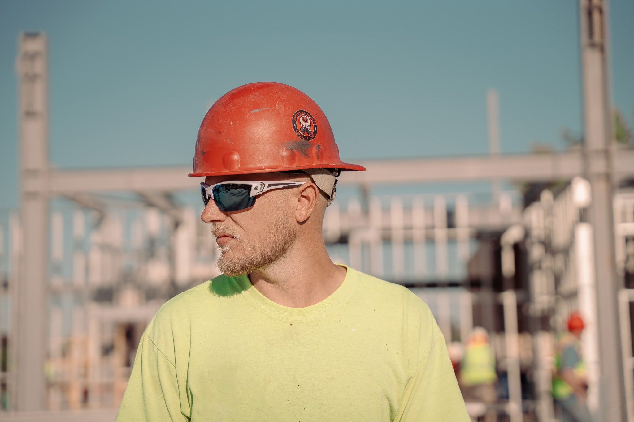 man wearing red hard hat and blue lens safety glasses in outdoor job site condition