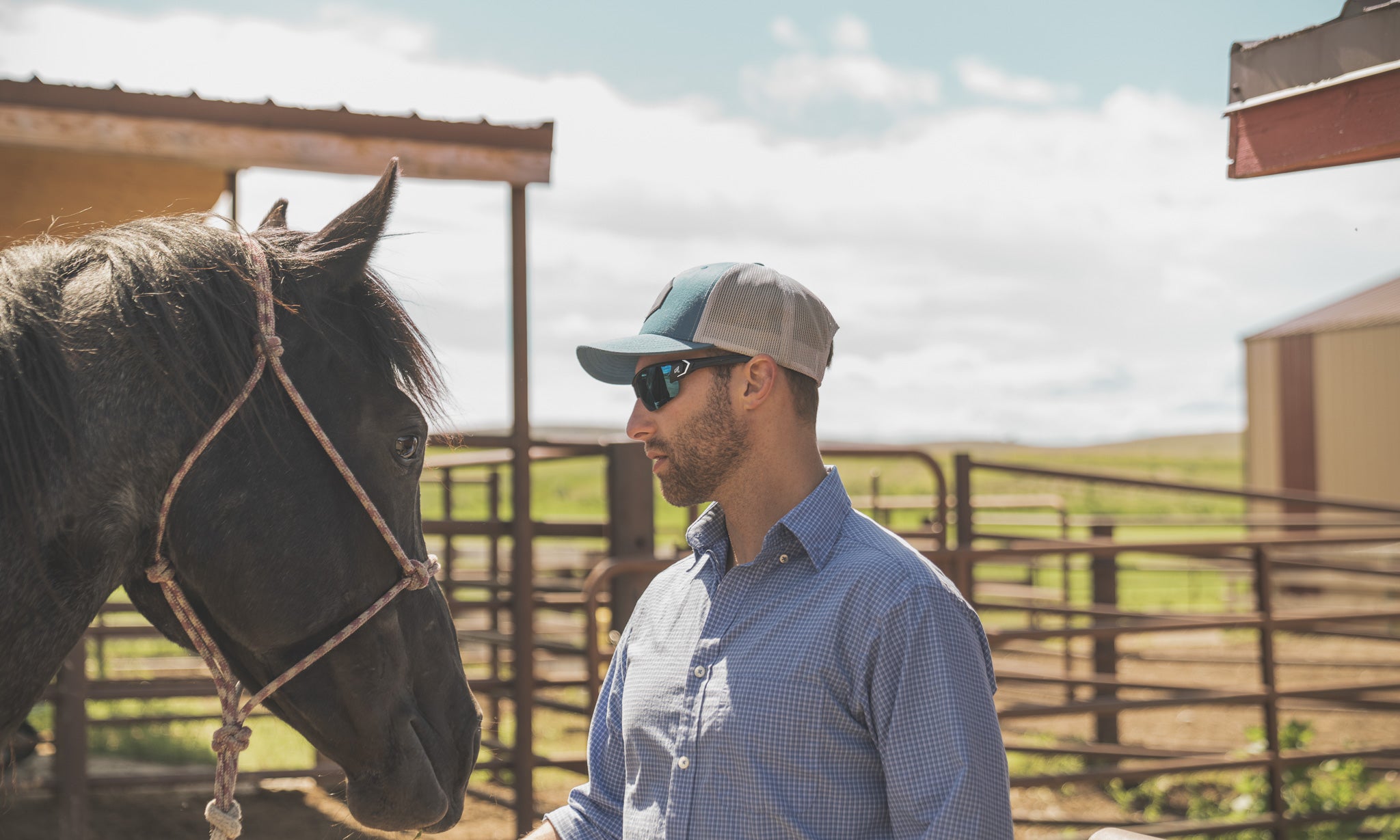 man wearing hat and safety sunglasses outdoors with a horse