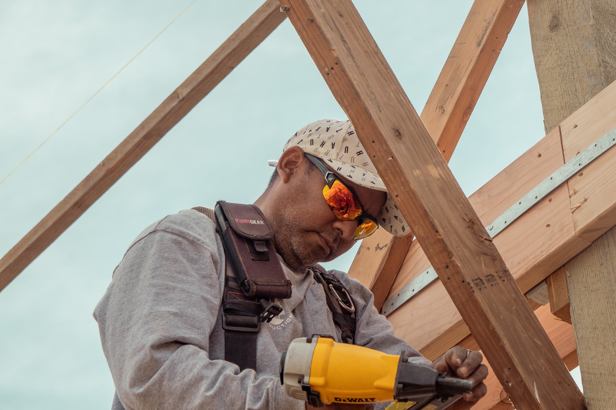 man working on wood structure with safety glasses and a hat on. 