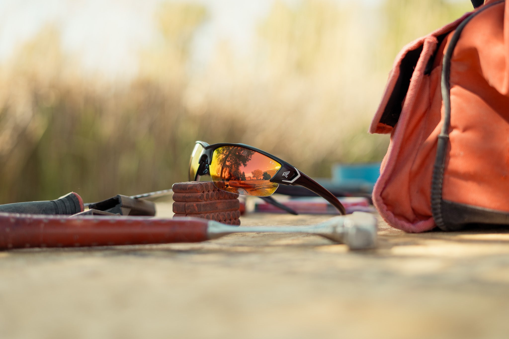 safety glasses with red lenses sitting among tools and other industrial supplies.