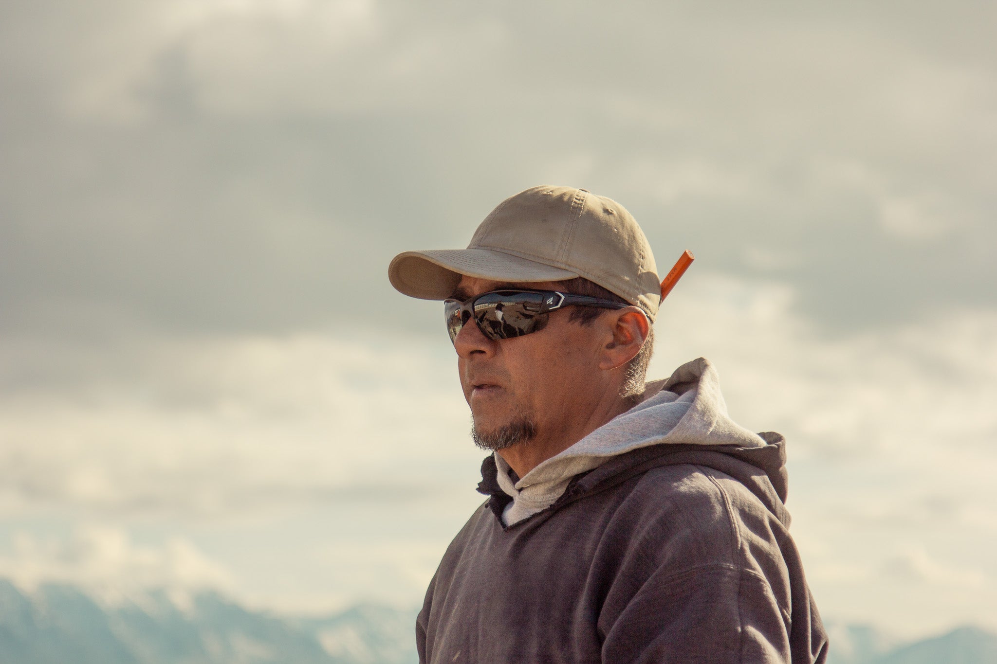 Man wearing safety sunglasses and a cap with mountains in the background