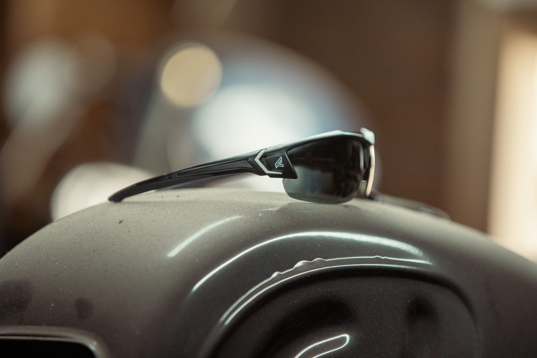 black lens safety glasses sitting on a motorcycle gas tank in a workshop setting.