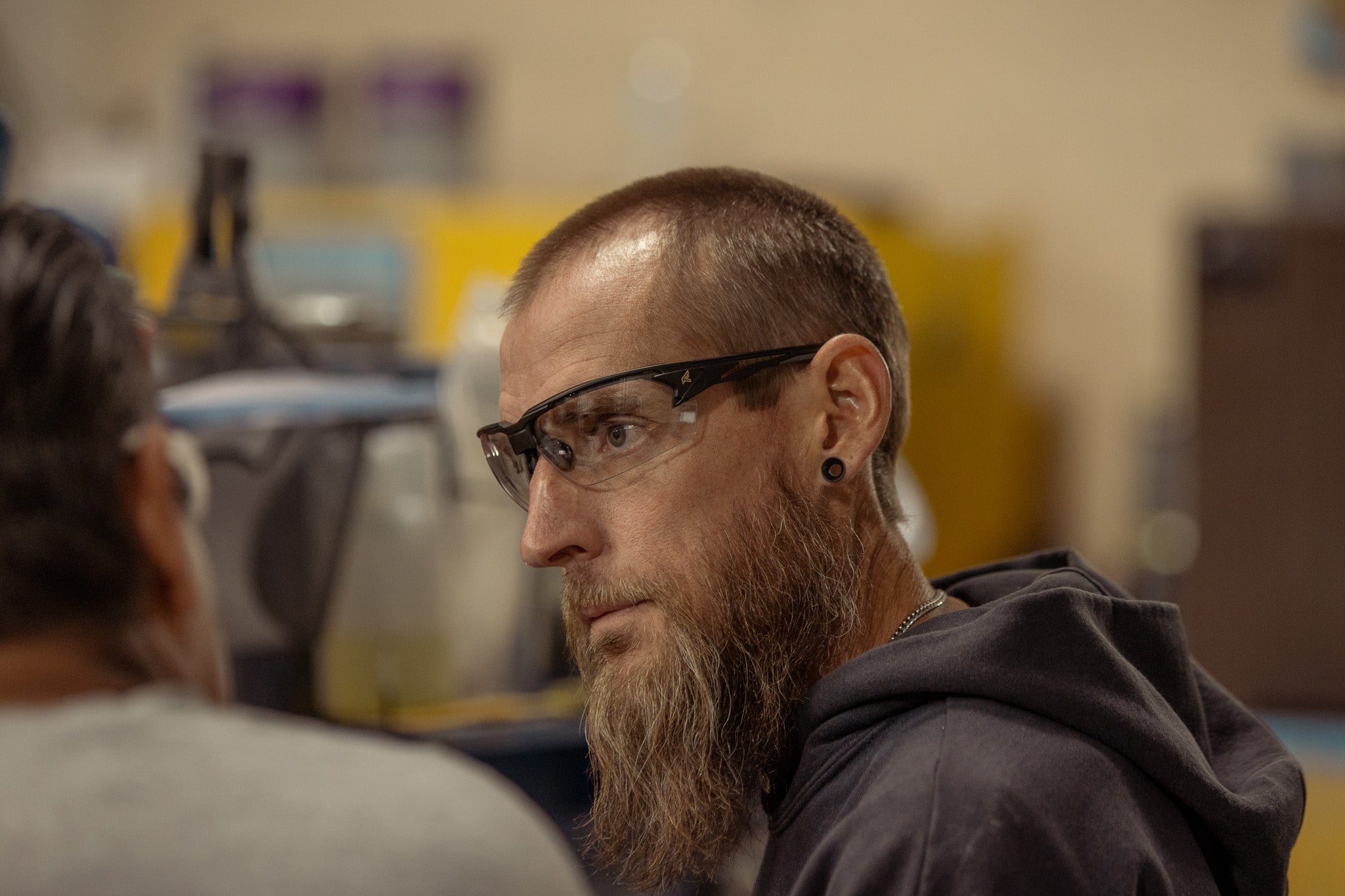 Man with a beard and safety glasses looking to the side in an industrial setting