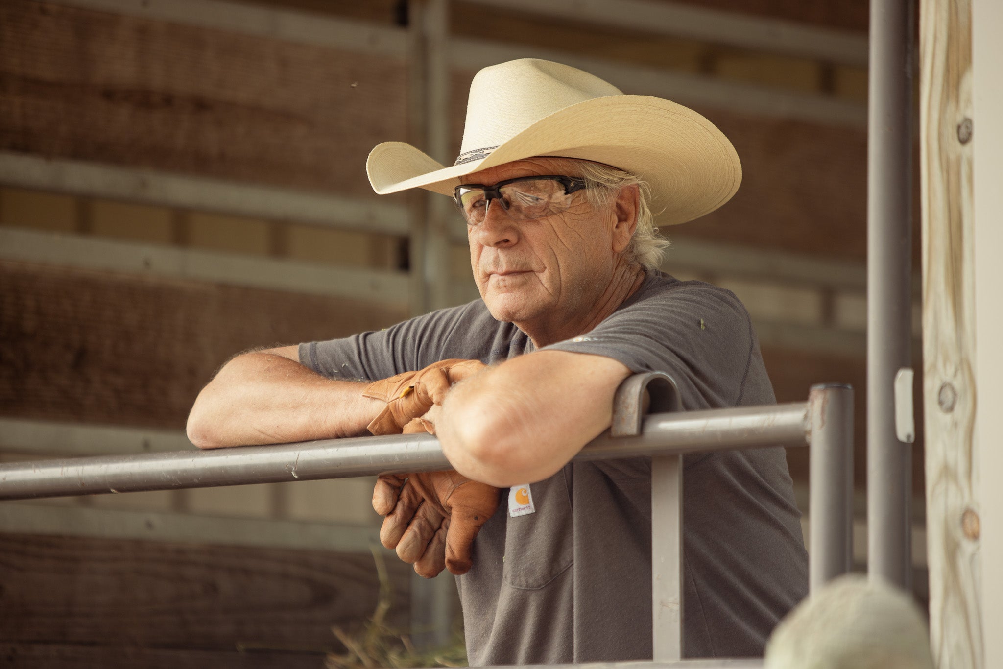 Man wearing a cowboy hat, safety glasses and Carhartt shirt in a barn setting
