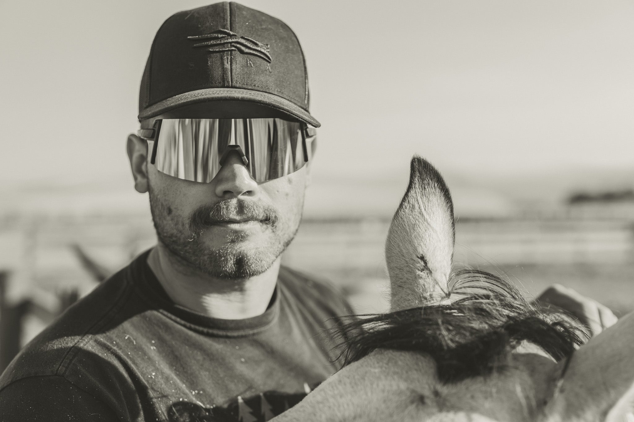 black and white photo of man with horse wearing a hat and sunglasses