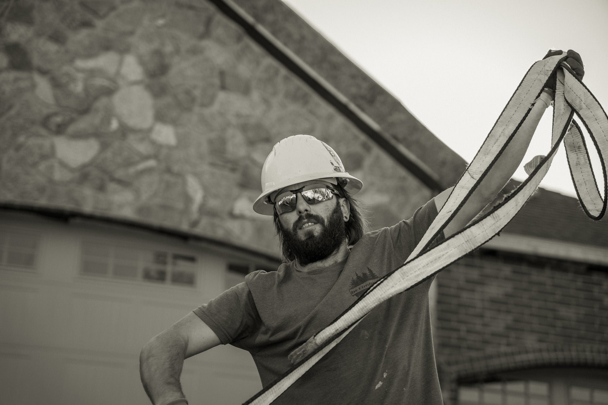 Person wearing a hard hat and safety glasses holding a large strap in front of a building.