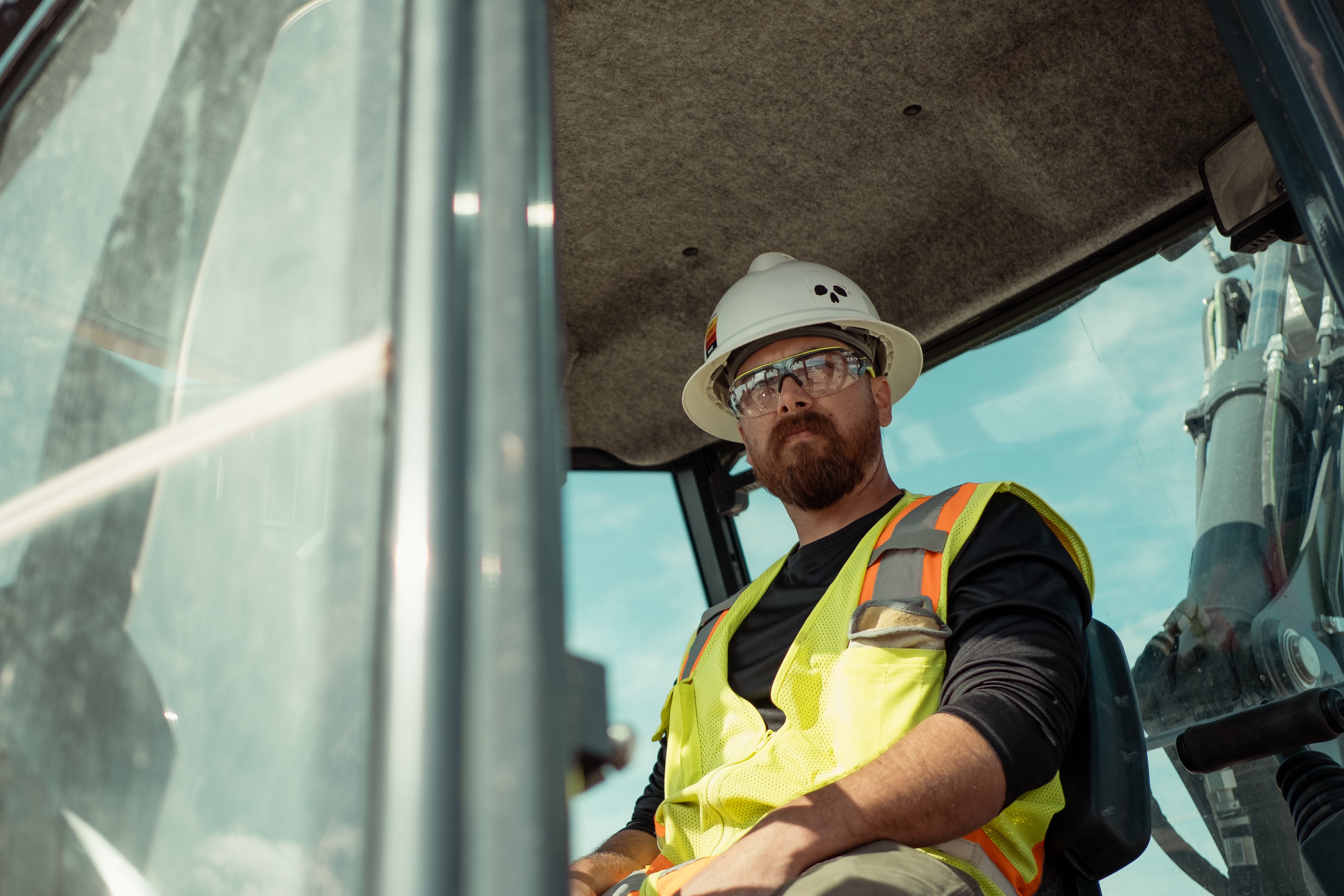 Man in high-visibility vest and hard hat sitting inside a large piece of machinery on a construction site.