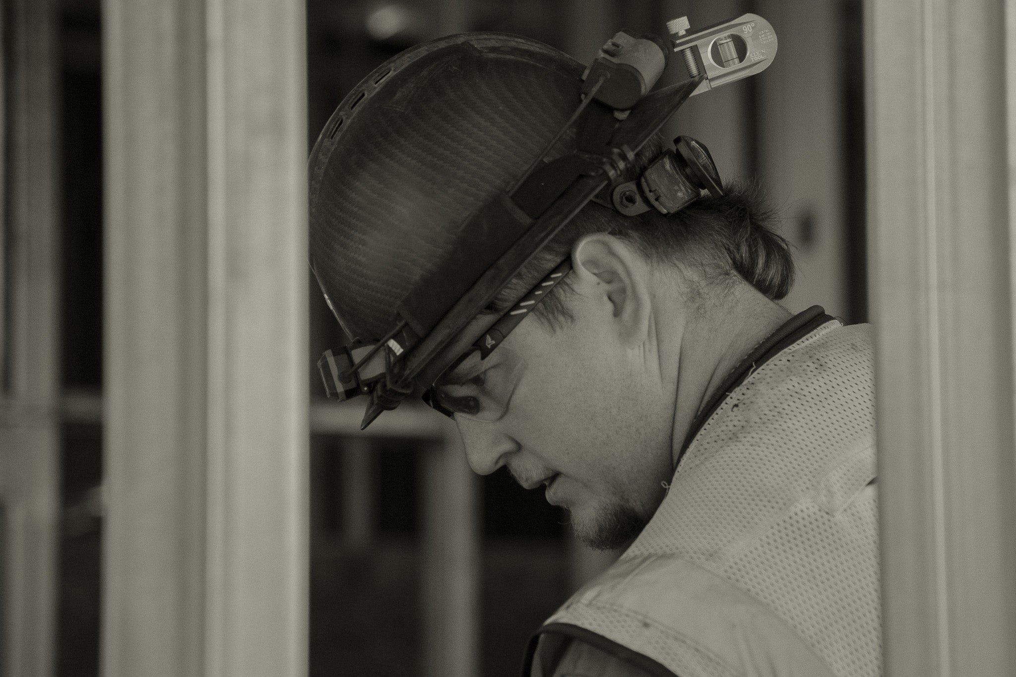 Person wearing a hard hat and safety glasses in a blurred indoor setting